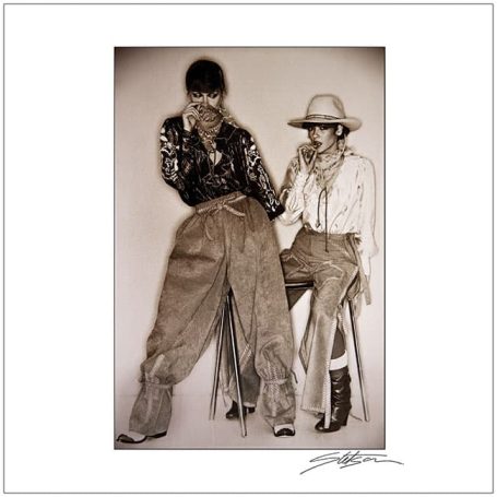 Two individuals in vintage Western attire, seated together, with one leaning forward.